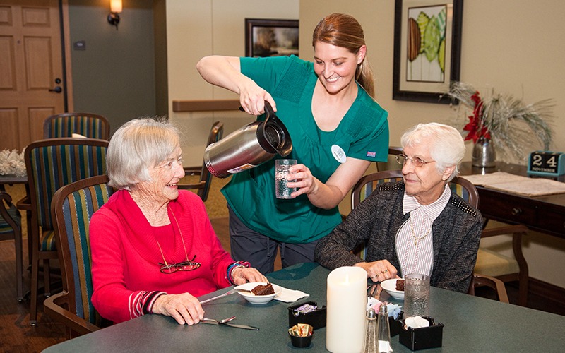 Staff member pouring coffee for two residents at Majestic Pines